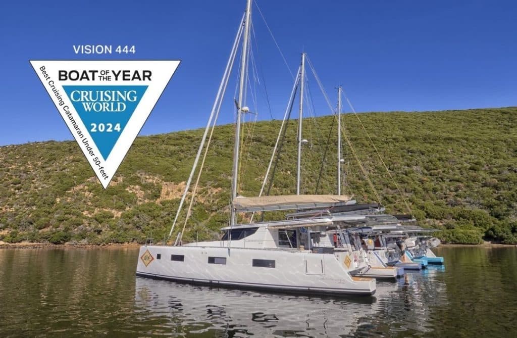 A lineup of Vision 444 catamarans anchored in calm waters, backed by green hills under a clear blue sky. A large badge in the top left corner displays “Boat of the Year 2024 – Cruising World” awarded for best cruising catamaran under 50 feet.